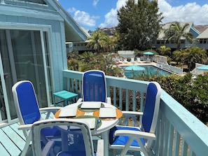 Een balkon met een tafel en stoelen, met uitzicht op een zwembadgedeelte met parasols en ligbedden.