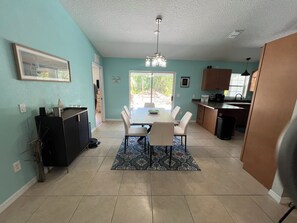 A dining area with a table, chairs, and a rug. There is a kitchen area with cabinets and a sink.