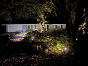 A house with a garage, surrounded by dense foliage and a small garden area.