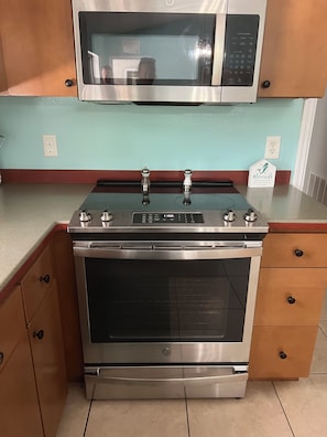 A kitchen with a stainless steel stove, oven, and microwave. There are wooden cabinets with black handles, a light blue wall, and a red countertop.