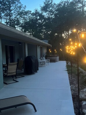 A covered outdoor patio with chairs, a barbecue grill, and string lights.