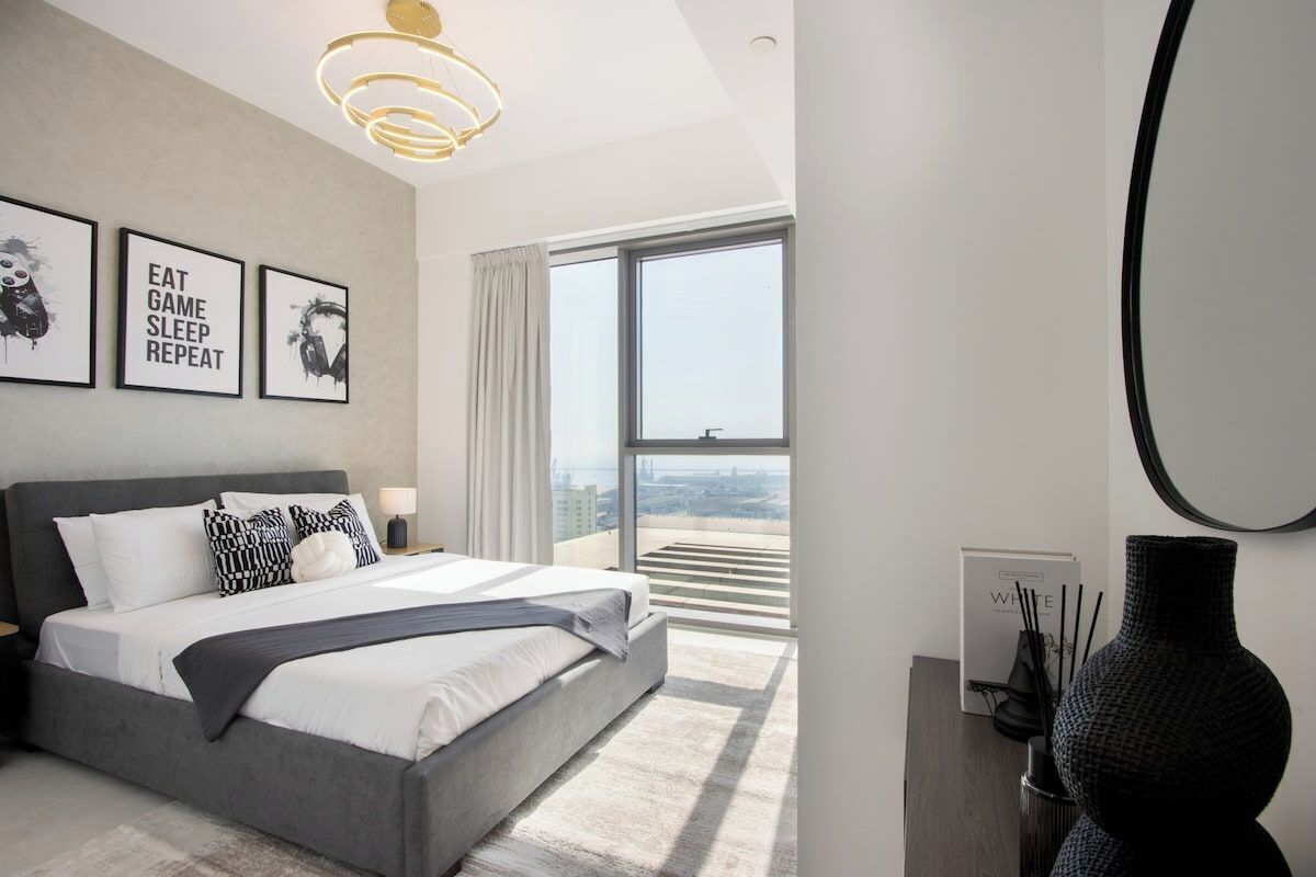 Ein modernes Schlafzimmer mit einem großen Bett, Blick auf die Stadt und drei gerahmten Motivationspostern.