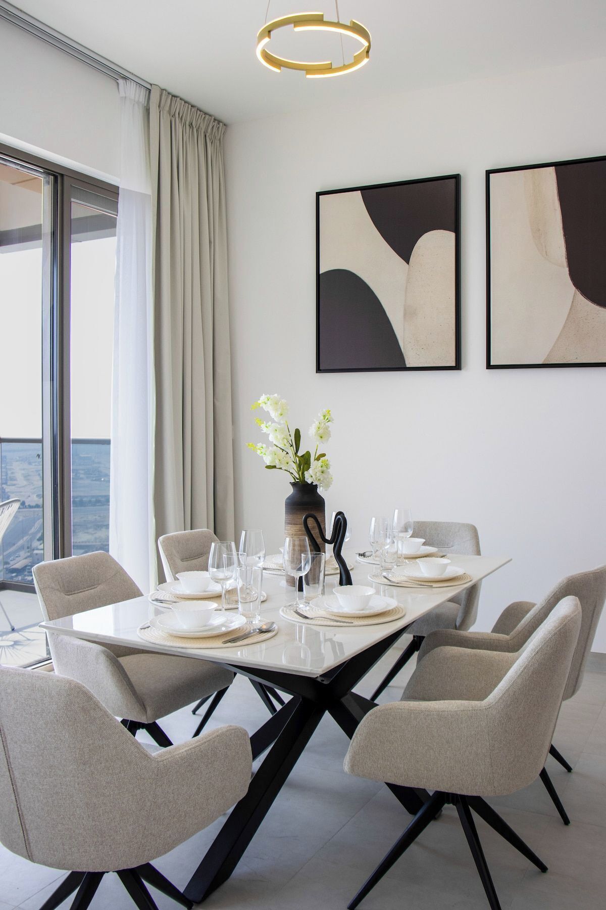 Ein modernes Esszimmer mit einem großen Tisch, gedeckt für sechs Personen, einer Vase mit weißen Blumen und abstrakter Kunst an der Wand.