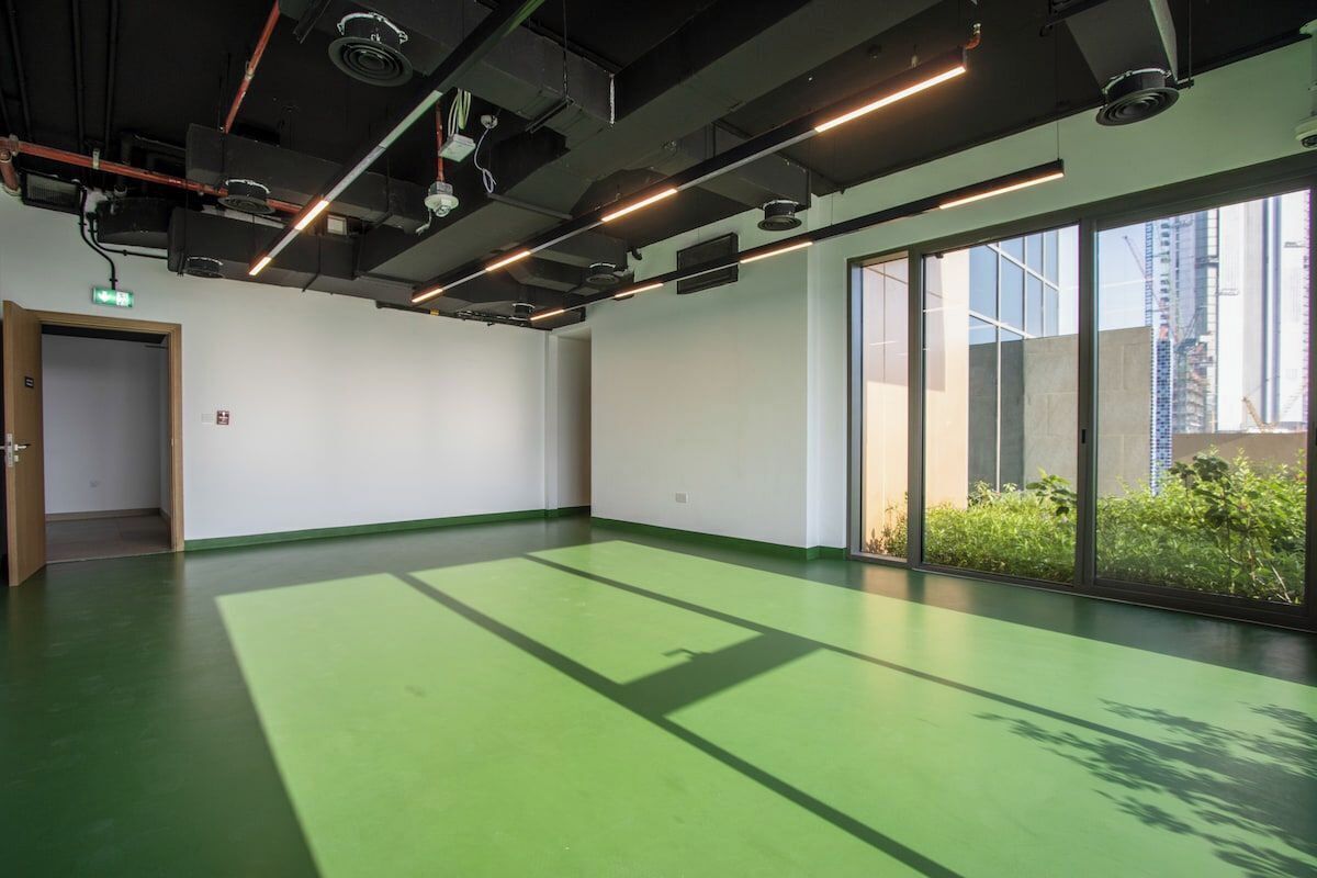 Um quarto amplo com piso verde, janelas grandes e vista para a cidade.