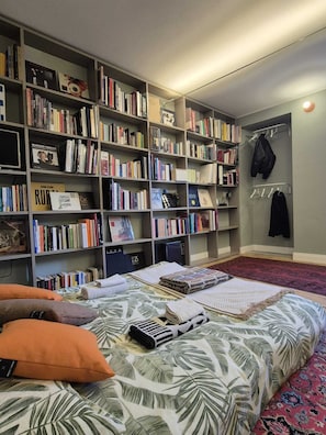 Una habitación con una amplia estantería, una cama con ropa de cama estampada y una alfombra roja.