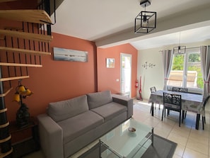 A living room with a sofa, a glass coffee table, a dining table with chairs, a staircase, and a painting on the wall. - A Little Provençal Paradise (Coccinelle Duplex) (Allemagne en Provence)