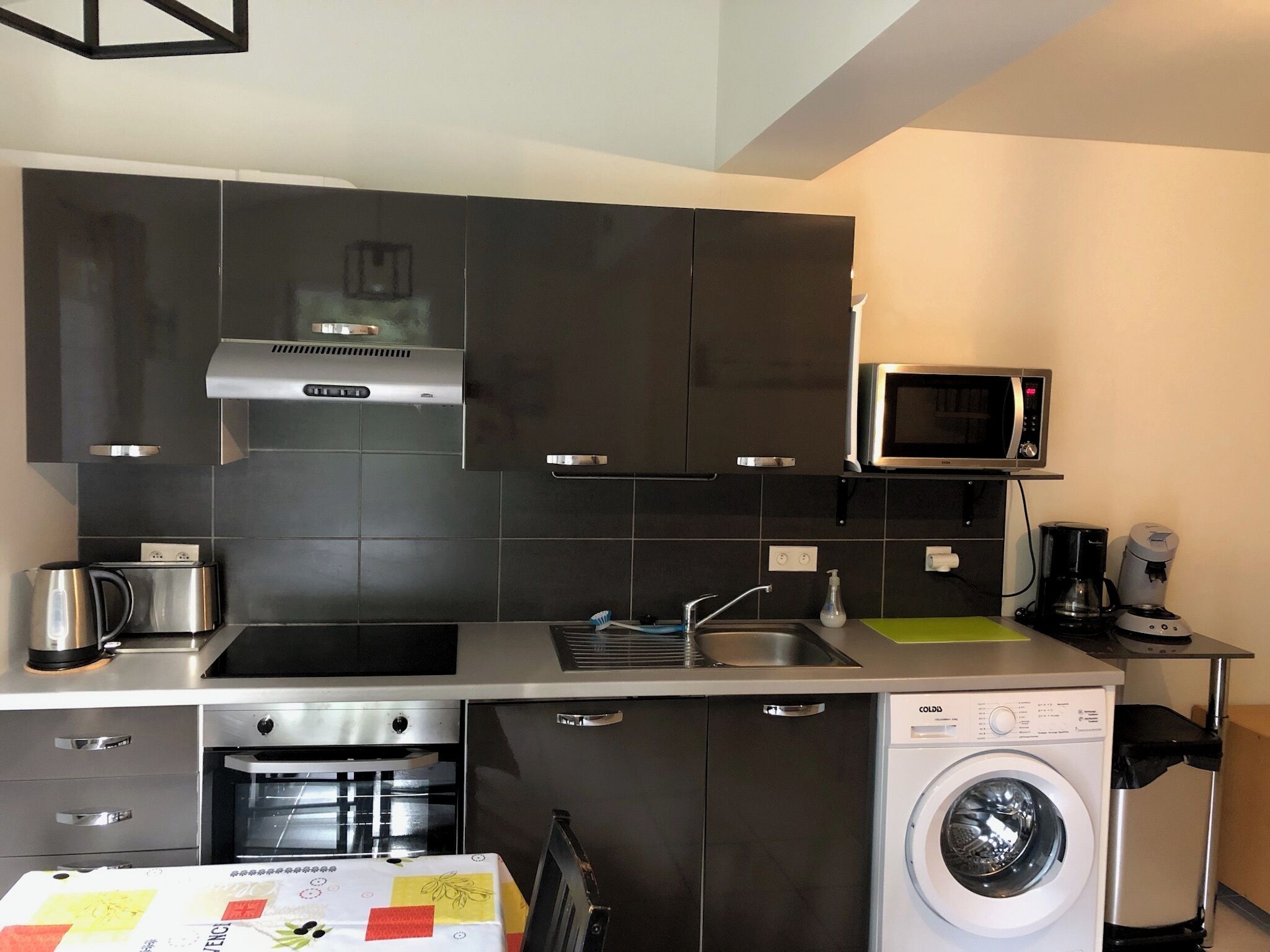 A compact kitchen with a microwave, coffee maker, and a washing machine.