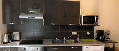 A compact kitchen with a microwave, coffee maker, and a washing machine.