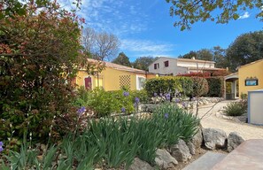 A courtyard with a yellow building, a white building, and a garden with purple flowers. - A Little Provençal Paradise (Coccinelle Duplex) (Allemagne en Provence)