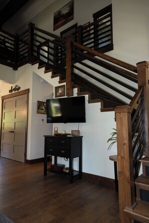 Eine Treppe mit Holzgeländern, ein an der Wand befestigter Flachbildfernseher und eine verschlossene Tür im Hintergrund.