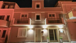 Un edificio de varios pisos con balcones, una puerta central y dos macetas.