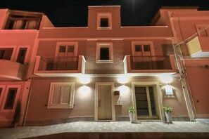 Un edifici de diversos pisos amb balcons, una porta central i dues plantes en testos.