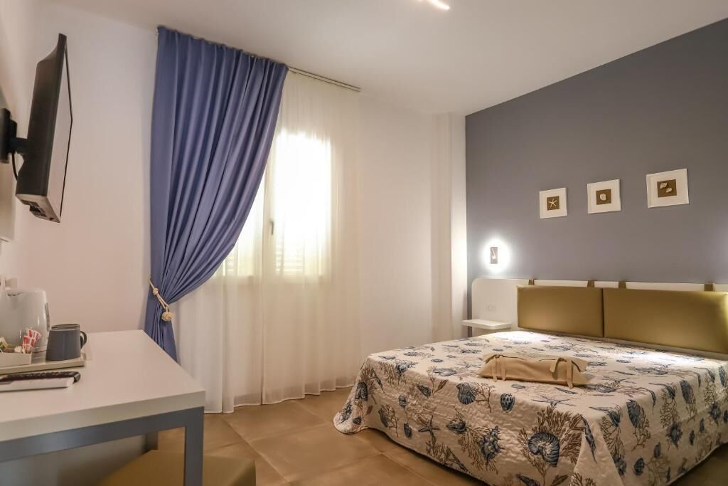 A bedroom with a bed, a desk, a TV, and curtains.