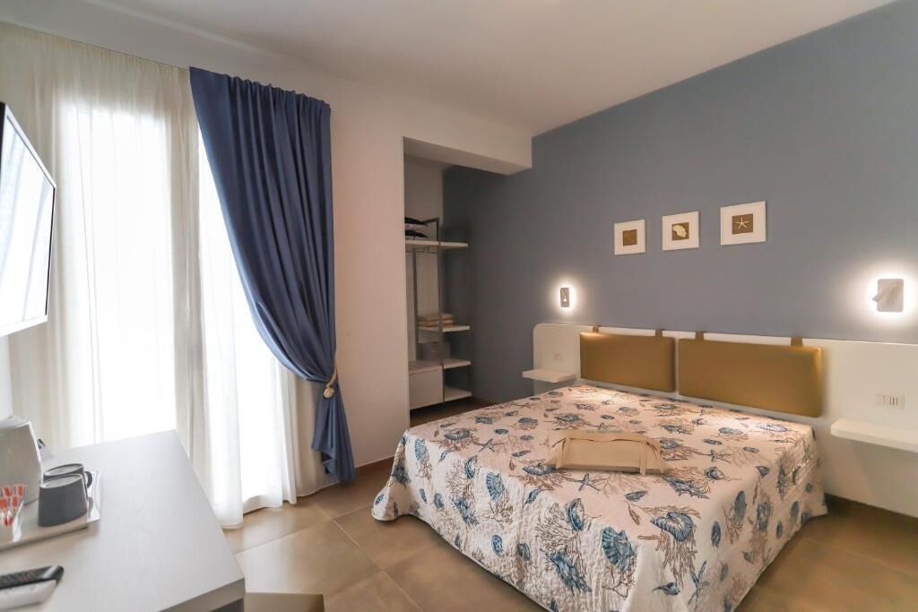 Une chambre à coucher comprenant un lit, des tables de chevet, un bureau, une chaise, une armoire et une fenêtre avec des rideaux.