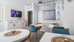 Una cocina moderna con televisor, armarios blancos y una zona de comedor con sillas azules.