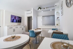 Eine moderne Küche mit Fernseher, weißen Schränken und einer Essecke mit blauen Stühlen.