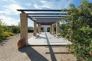 Un patio esterno con colonne in pietra, panche di legno e una struttura a pergola.