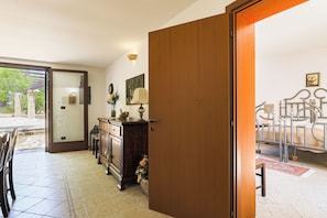 A room with a wooden door, a dining area with chairs and a table, a cabinet with decorative items, and a bed with a metal frame. - Uva Regina by Casa di Marco (Gallipoli)