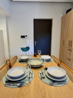 A dining table set with plates, glasses, and cutlery, flanked by wicker chairs, with a door and a cabinet in the background.