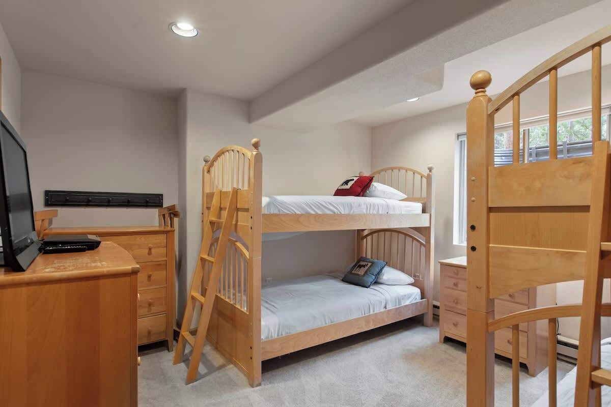 A bunk bed room with a desk, drawers, and a TV.
