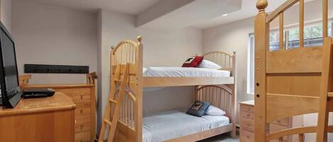 A bunk bed room with a desk, drawers, and a TV.