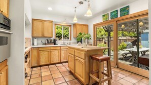 A kitchen with wooden cabinets, a central island, and a bar stool. - The Point House steps to Pleasure Point! (Santa Cruz)