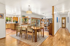 Eine geräumige Küche mit Holzausstattung, ein Essbereich mit großem Holztisch und Stühlen sowie eine Bibliothek mit Bücherregalen.
