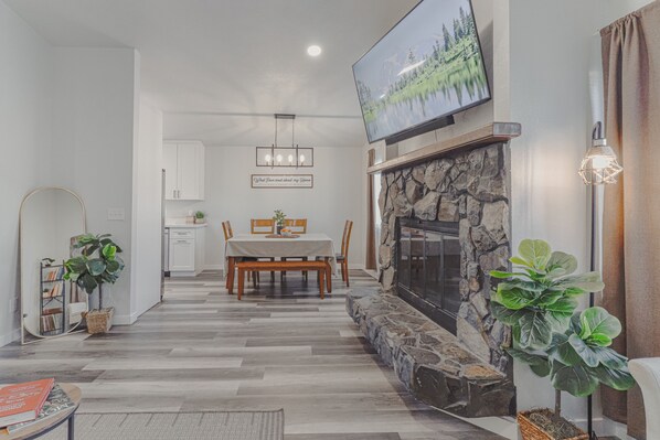 A modern living room with a fireplace, a dining area, and a flat-screen TV mounted above the fireplace.