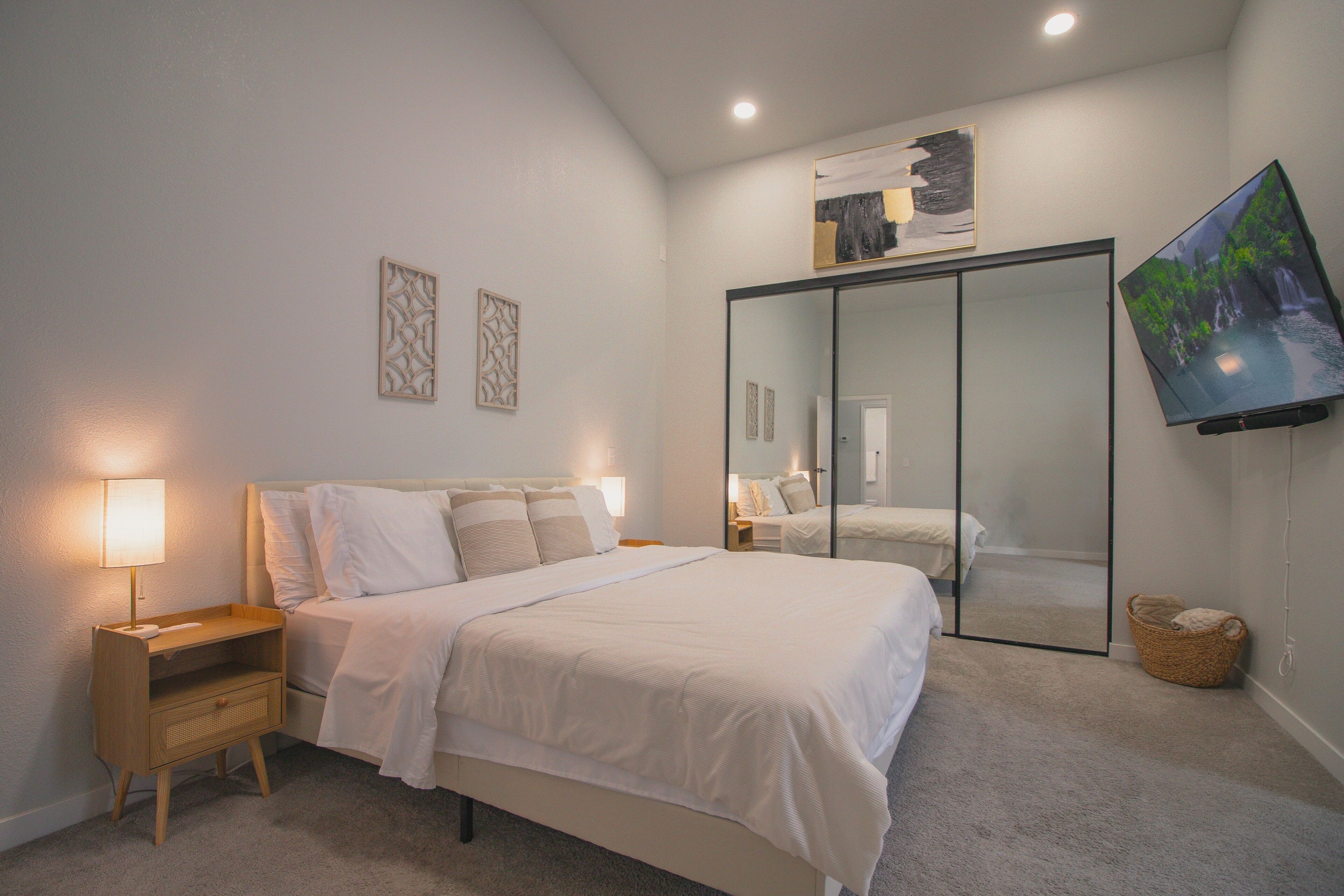 Quarto com cama, mesas de cabeceira, televisão, guarda-roupa e espelho.