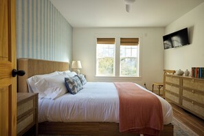 A bedroom with a bed, bedside tables, a dresser, a television, and a window with blinds.