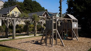 A playground with wooden structures, including a swing set and a climbing frame, surrounded by a gravel area. - Beach Walk, Hot Tub, Pool, Gym, Fire Pit, Games, Sleeps 13 (Lincoln City)