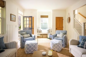 A cozy living room with two sofas, a coffee table, and a bench. There is a window with a view of the outside, a door, and a staircase. - Beach Walk, Hot Tub, Pool, Gym, Fire Pit, Games, Sleeps 13 (Lincoln City)