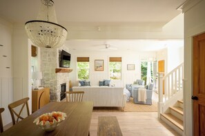 A spacious living room with a fireplace, a dining area with a wooden table, and a staircase leading to an upper level.