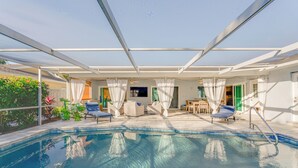 Una piscina interior con agua azul cristalina, rodeada de cortinas blancas y equipada con sillones de descanso y una mesa.