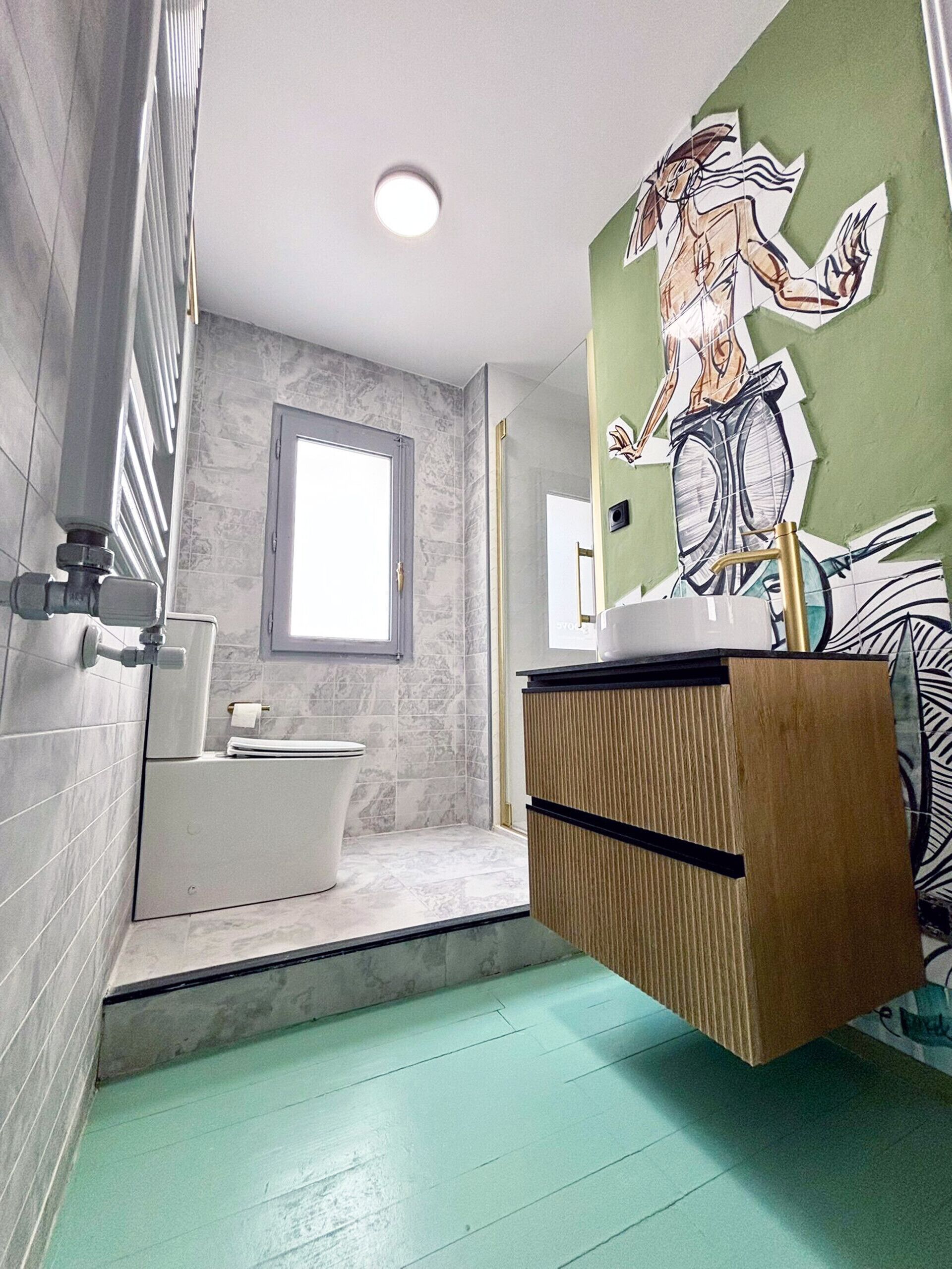 Et badeværelse med toilet, vask med spejl og en væg med et mural.