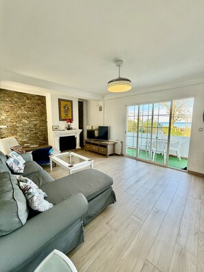A living room with a grey sofa, a fireplace, a television, and a view of the outdoors through large windows. - Beachfront Paradise By Gloove (Denia)