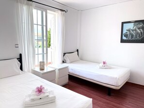 Ein Hotelzimmer mit zwei Betten, einem Fenster mit Vorhängen, einem Nachttisch und einem gerahmten Bild an der Wand.