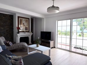 Ein Wohnzimmer mit Kamin, Fernseher, einer Couch und einem großen Fenster.