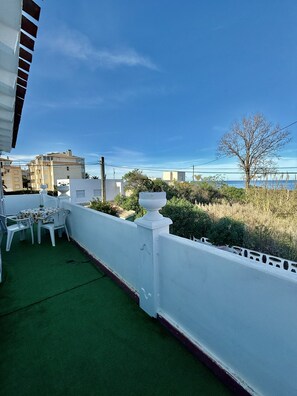 Una terraza en la azotea con césped artificial verde, barandilla blanca y vistas al mar y edificios al fondo.