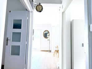 Ein Flur mit einer weißen Tür, einer Uhr und einem runden Spiegel an der Wand.