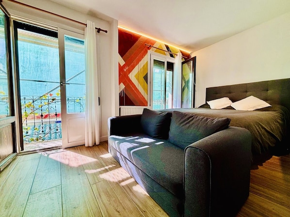 Ein modernes Schlafzimmer mit einer Schlafcouch, einem Bett und Blick auf einen Balkon mit Pflanzen.