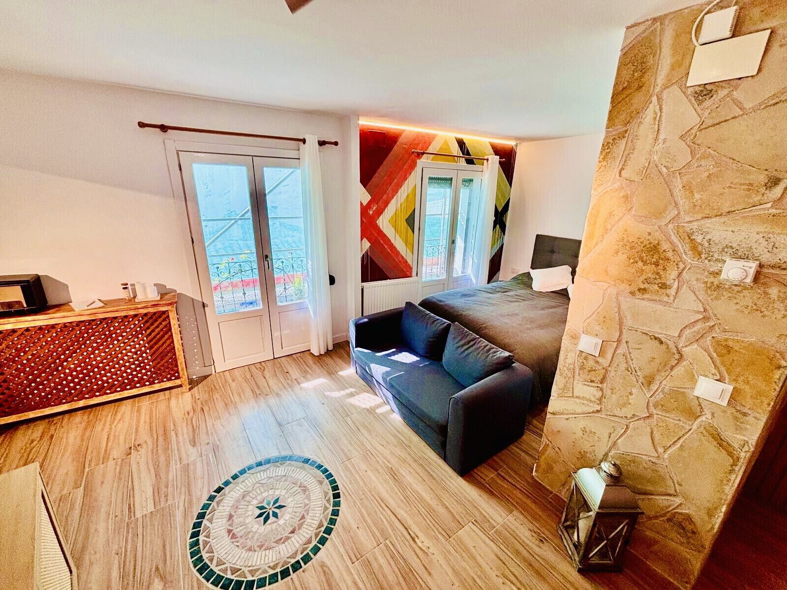 Una habitación con piso de madera, un sofá, una mesita y una pared con diseño geométrico, junto a una pared de piedra.