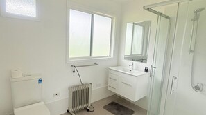A bathroom with a toilet, a radiator, a sink, a mirror, and a shower. - Prom Coast Residence (Fish Creek)
