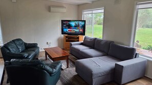 A living room with a grey sofa, a black leather chair, a wooden coffee table, and a TV on a wooden stand. - Prom Coast Residence (Fish Creek)