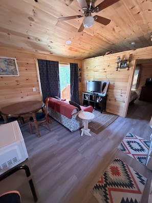 A wooden cabin interior with a bed, TV, and dining area.
