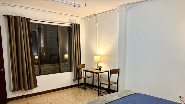 Habitación de hotel con cama, escritorio con sillas, ventana con cortinas y lámpara.