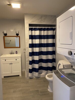 Ein Badezimmer mit gestreiftem Duschvorhang, Waschbecken, Spiegel, Toilette und Waschmaschine.