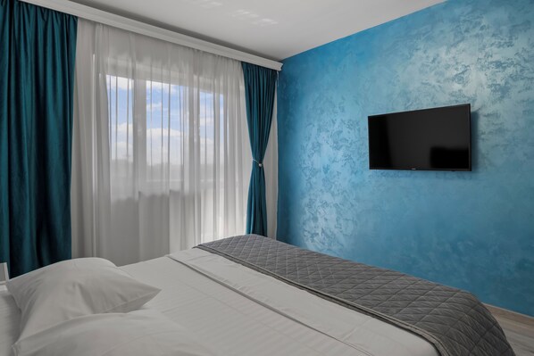 Une chambre d’hôtel avec un lit, des rideaux, un téléviseur fixé au mur et une fenêtre.