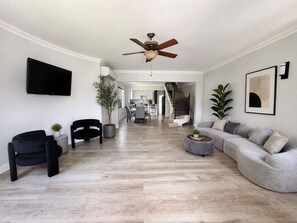A modern living room with a flat-screen TV, a ceiling fan, and a staircase leading to an upper level. - Upscale Caribbean Retreat with Oceanview Balcony & Resort Style Living (Montego Bay)