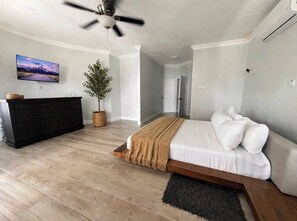 A modern bedroom with a bed, a dresser, a television, and a ceiling fan. - Upscale Caribbean Retreat with Oceanview Balcony & Resort Style Living (Montego Bay)